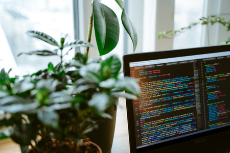 Html code on the laptop screen standing on a wooden table with home green plants, cozy working...