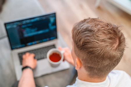 Top view of a young male programmer drinking coffee and writing on a laptop keyboard. The concept of...