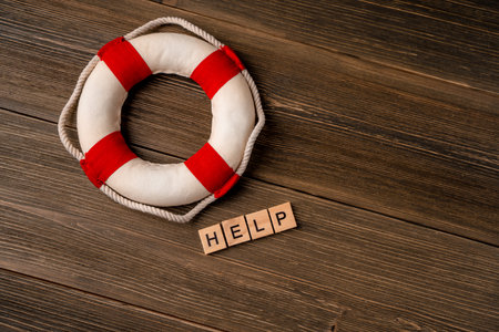 A lifebuoy next to the letters "help" made of wooden blocks on a wooden table. Support conceptの写真素材