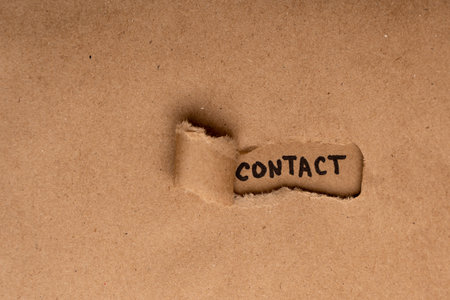 Kraft paper with a hole where it is written with a marker "Contact". Background for the site for navigating the organization's contactsの写真素材