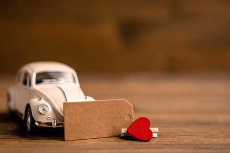 A toy white car with a heart with a piece of paper for notes on a wooden background. Creative place for textの写真素材