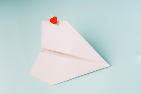 A paper airplane with a heart-shaped clothespin on a blue background. The concept of a love message. Valentine's Day, love noteの写真素材