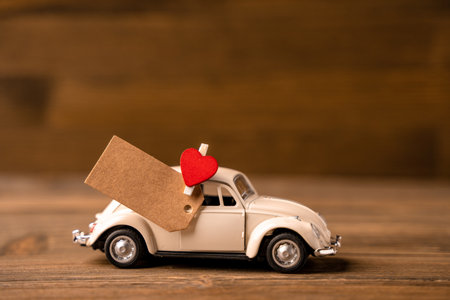 A toy white car with a heart with a piece of paper for notes on a wooden background. Creative place for textの写真素材