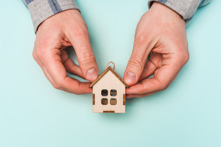 Men's hands embrace a wooden house as a symbol of careの写真素材