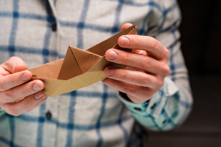A man holds a craft paper boat in his handsの写真素材