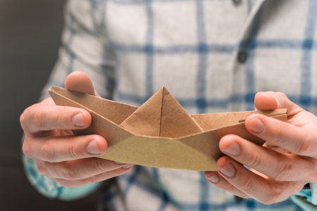 A man holds a craft paper boat in his handsの写真素材