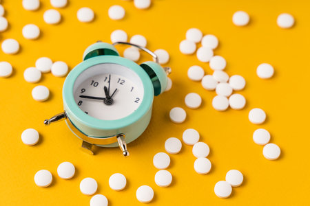The alarm clock is lying on a yellow background in the middle of the scattered pills. The concept of...