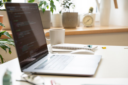 The laptop on a white desk in a bright office, the code on the screenの写真素材