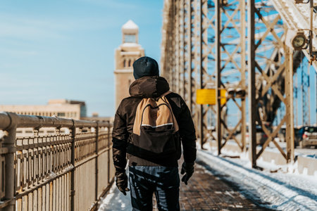 A young man in a jacket walks on a snow bridge in Saint Petersburg in winter in sunny weather