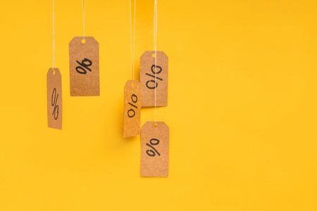 Tags with drawn percentages hang on strings on a yellow background, concept of discounts and salesの写真素材