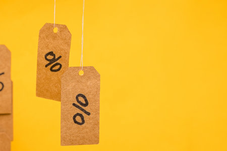 Tags with drawn percentages hang on strings on a yellow background, concept of discounts and sales
