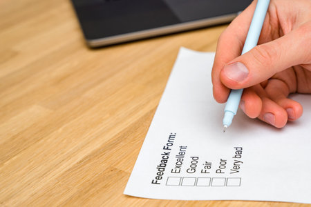 A questionnaire with answer options for the feedback form. A man ticks a box on a white paper while sitting at a wooden table. Checking the form of the check box.の写真素材