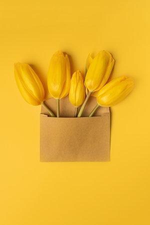 Top view of yellow tulips in envelope on yellow background. Valentine's, mother's day or spring mockup with white cardの写真素材