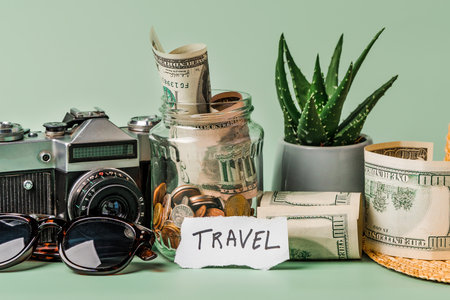 A glass jar with coins and the inscription "travel" on a pastel background with space for text. The concept of saving money for travelの写真素材