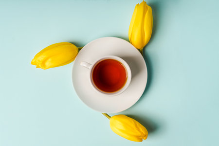 A mug of tea and yellow tulips on a blue background. Spring composition with flowers, place for textの写真素材