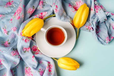 A mug of tea and yellow tulips on a blue background. Spring composition with flowers, place for textの写真素材