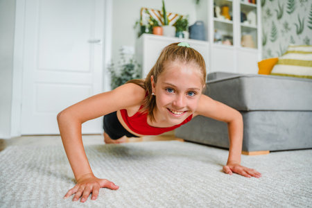 A cheerful little girl does yoga on the carpet at home, doing fitness exercises at home. Home remote...