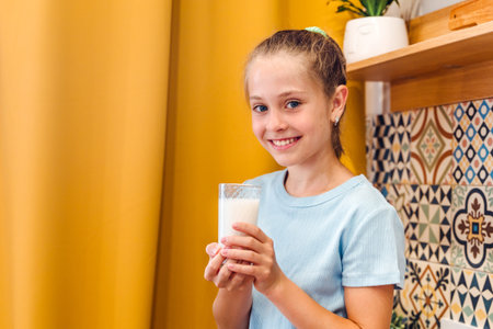 A beautiful little girl is having fun drinking a glass of fresh milk against a white brick wallの写真素材