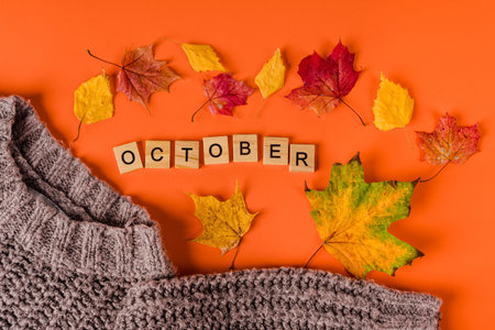Autumn background with leaves and a warm sweater, the word "October" is made of wooden letters on an orange backgroundの写真素材