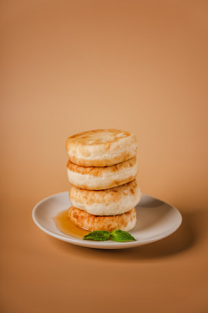 Cottage cheese pancakes on a plate with honey and mint on a beige background. Healthy and delicious morning breakfast. Traditional Russian food. Copyspace.の写真素材