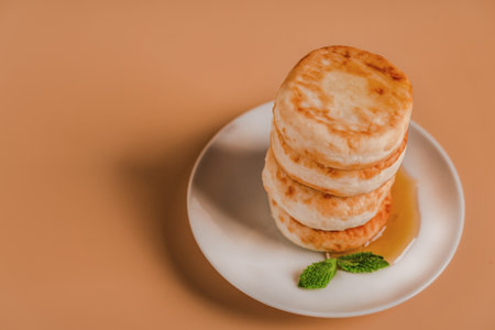 Cottage cheese pancakes on a plate with honey and mint on a beige background. Healthy and delicious morning breakfast. Traditional Russian food. Copyspace.の写真素材