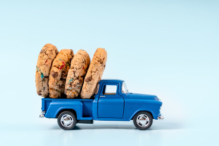 A toy car carries cookies with chocolate and cinnamon sticks on a blue background. Holiday card for New Year and Christmasの写真素材