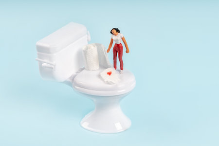 A miniature model of a woman stands near a toy toilet with toilet paper with blood. The concept of hemorrhoidsの写真素材