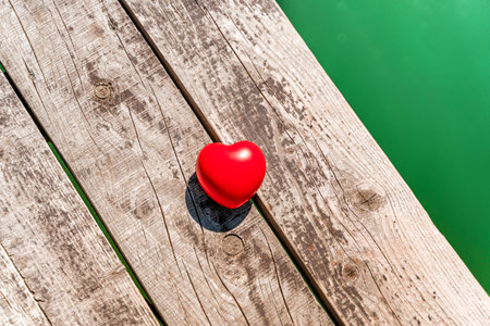 The red heart lies on a wooden pier on the lake. Beautiful summer concept of a serene holiday.の写真素材