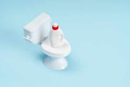 A miniature toilet bowl and a bottle of cleaning agent on a blue background. Objects in minimalism