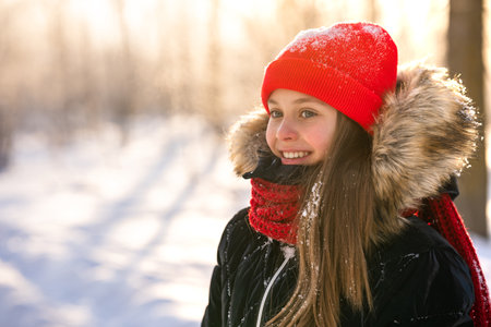 A little girl in a red hat and scarf walking through a winter forest with snow-covered trees. beautiful winter landscape.の写真素材