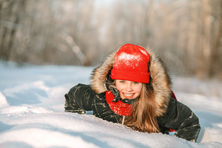 A little girl in a red hat and scarf walking through a winter forest with snow-covered trees. beautiful winter landscape.の写真素材