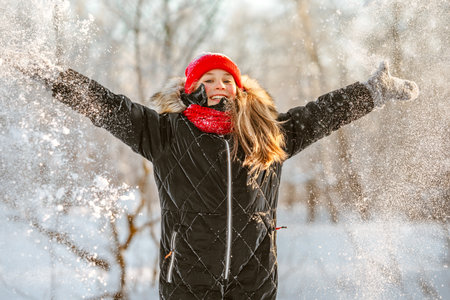A little girl in a red hat and scarf walking through a winter forest with snow-covered trees. beautiful winter landscape.の写真素材