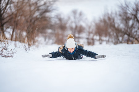 A little girl in a warm suit holds a tray for skating down an ice slide in winter. Winter fun in the snow.の写真素材