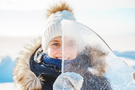 Portrait of smiling little girl looks through a transparent piece of ice on a frosty winter dayの写真素材