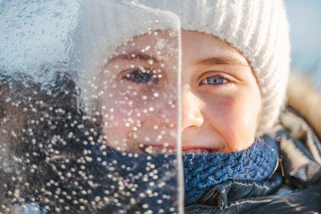 Portrait of smiling little girl looks through a transparent piece of ice on a frosty winter dayの写真素材
