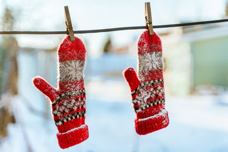 Red knitted mittens dusted with snow hang on wooden clothespins against the background of a winter landscape on a clear day. cute winter conceptの写真素材