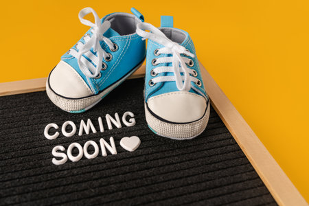 Tiny baby's sneakers and a board with the inscription "coming soon". Pregnancy concept and expecting babyの写真素材
