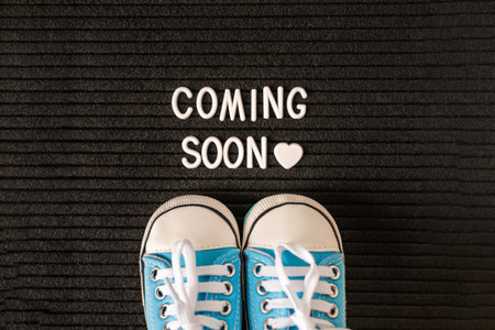 Tiny baby's sneakers and a board with the inscription "coming soon". Pregnancy concept and expecting babyの写真素材