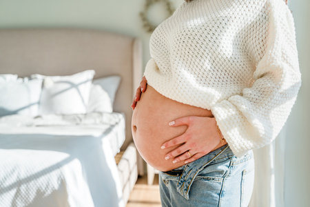 A beautiful young pregnant woman in a bright modern interior. Tender concept of motherhood, pregnancy and baby waitingの写真素材