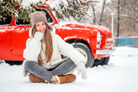Beautiful young woman sitting on the snow near the old car.の写真素材