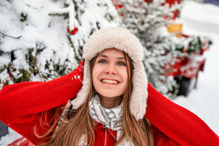 Portrait of a beautiful girl in a red sweater and a white hat on the background of the Christmas...