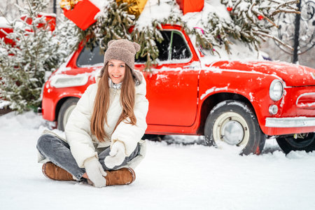 Beautiful young woman sitting on the snow in front of red carの写真素材