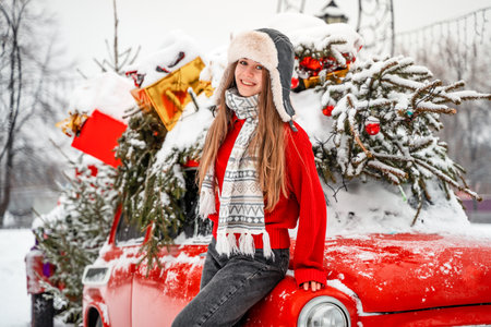 A beautiful young woman in a winter hat with earflaps next to a retro red car decorated for...