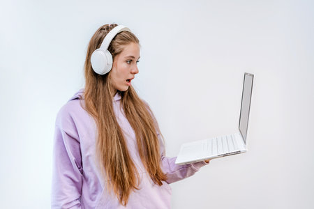 A surprised and scared teenage girl in a purple hoodie and headphones stands with a laptop on an...