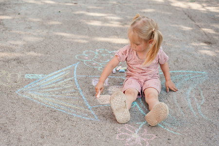 A little child girl draws a house and a tree on the asphalt with chalk, a childhood concept and...