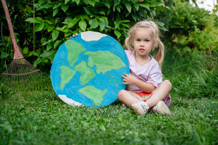 A little child girl holds a drawing on the cardboard of planet earth outdoor, a concept of the environment and ecologyの写真素材