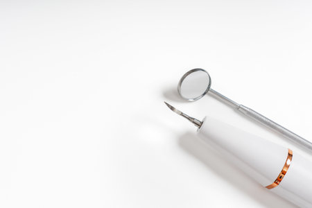 A dental mirror and a handpiece tool neatly placed on a white background, showcasing professional dental equipment.の写真素材