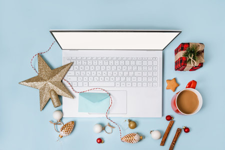 Top view of a laptop on a table with an isolated blue background for mockup flat lay in Christmas time. Christmas tree, gifts, decorations in background. New year concept in office.の写真素材