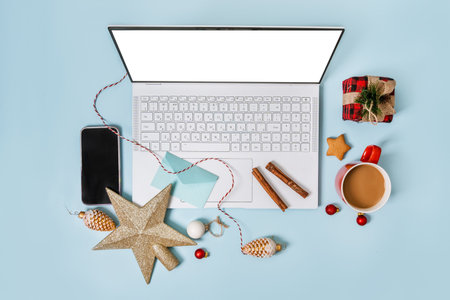Top view of a laptop on a table with an isolated blue background for mockup flat lay in Christmas time. Christmas tree, gifts, decorations in background. New year concept in office.の写真素材