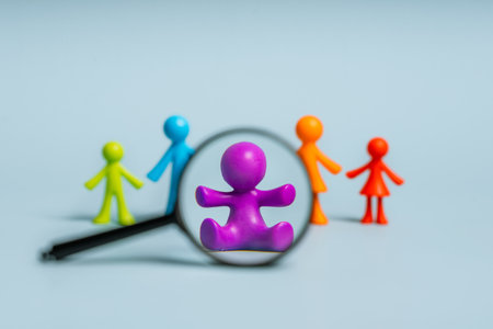 Multicolored figures of little men, a family on an isolated blue background, in the foreground highlight a baby, the concept of a second or third child with a magnifying glassの写真素材